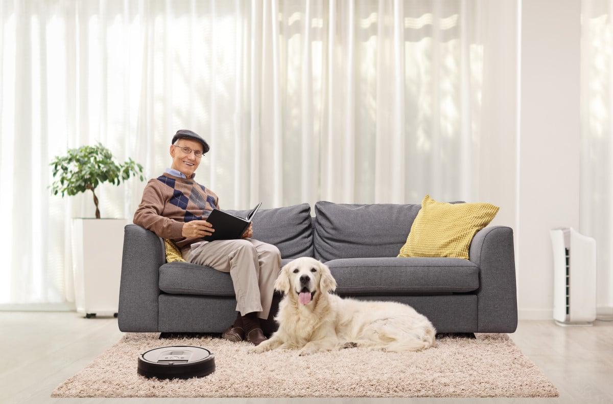 一位老人坐在客厅的沙发上，地毯上放着一只金毛猎犬